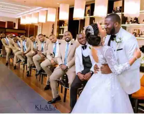 Groomsmen Staring As Groom Kisses His Bride In Adorable Photo